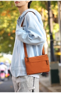 Detailed view of an orange nylon crossbody bag worn over a blue hoodie in outdoor setting