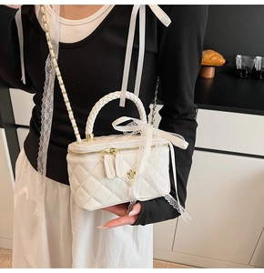 Detail of white quilted mini box bag with lace bow and chain strap on a table