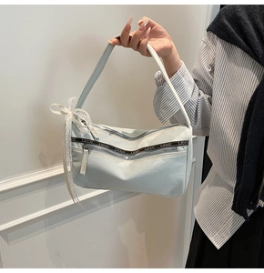 Detail of light blue denim baguette bag featuring ribbon branding and lace bow accent