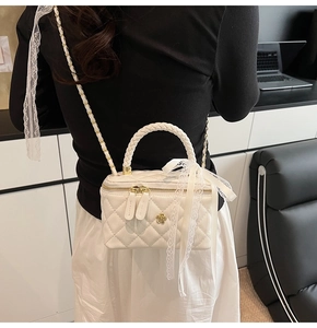 White quilted box bag with gold flower charm and lace ribbon on a chain strap