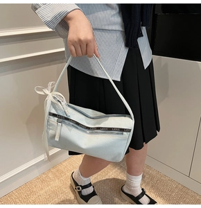 Detail of light blue denim baguette bag with lace bow accessory and double zippers