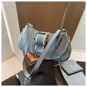 Detail of light blue denim underarm bag featuring frayed edges and a large metal buckle