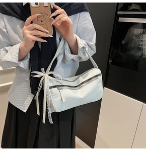 Detail of light blue denim baguette bag with white lace bow and woven alphabet strap