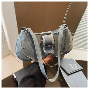 Detail of light blue denim baguette bag featuring frayed edges and silver buckle closure