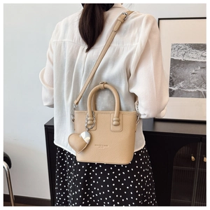 Detail der beigen Bucket-Bag mit Litschi-Muster und Herzanhänger an einem Model
