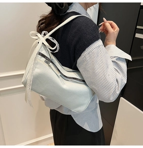 Detail of light blue denim baguette bag with lace bow and branded zipper strap