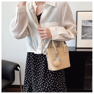 Detailansicht der beigen Eimer-Handtasche mit Herzanhänger getragen vom Model