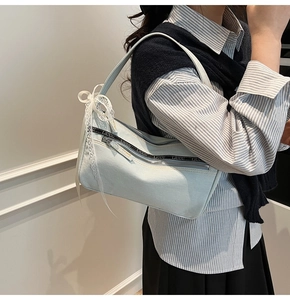Detail of light blue denim baguette bag featuring silver zippers and white lace bow