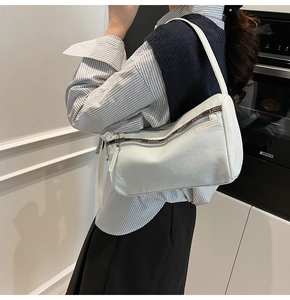 Detail of light blue denim baguette bag featuring double zippers and brown logo webbing