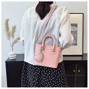 Rosa Eimertasche mit Lederstruktur und Herzanhänger getragen von einem Modell