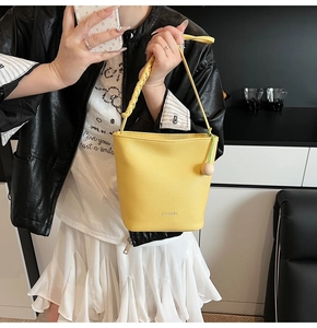 Detail of yellow bucket bag with lychee texture, woven handle and wooden bead charm