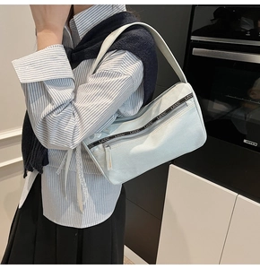 Detail of light blue denim baguette bag featuring decorative zipper and branded strap