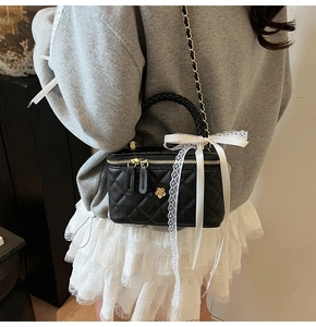 Detail of black quilted box bag with gold chain and white lace bow accessory