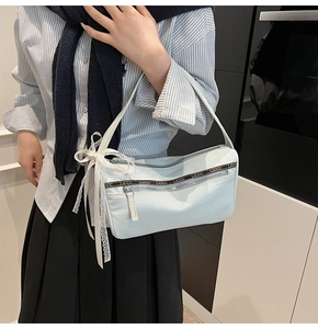 Detail shot of light blue denim bag featuring stylish side white lace ribbon bow and zippers