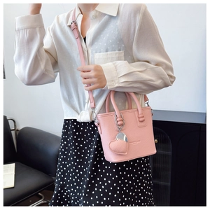 Detail der rosa Mini-Eimertasche mit Herzanhänger getragen mit weißem Hemd und gepunktetem Rock