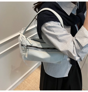 Detail of light blue denim baguette bag featuring decorative zippers and lace bow details