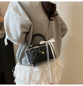Detail of black quilted mini bag featuring golden hardware and elegant lace bow decoration