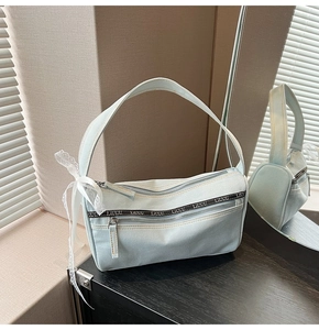 Detail of light blue denim baguette bag featuring ribbon print and lace bow accessory