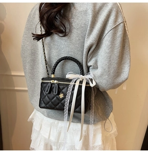 Detail of black quilted box bag with gold flower buckle and white lace bow accessory