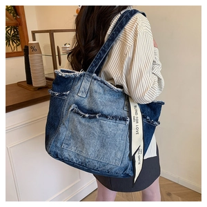 Détail du sac cabas en denim contrasté avec bords effilochés et ruban logo décoratif