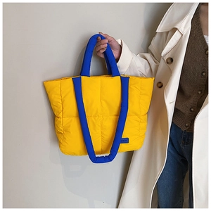 Détail d'un sac cabas matelassé jaune avec anses bleues et étiquette de mode sur le devant