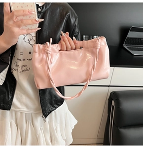 Detail of a pink glossy faux leather handbag featuring a braided strap and pleated opening