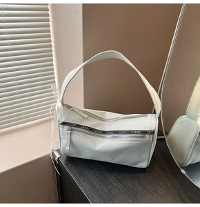 Detail of light blue denim baguette bag with lettered webbing and white lace bow