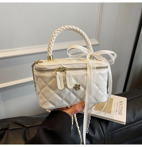 Detail of white quilted bag featuring woven handle, lace bow, and gold flower hardware