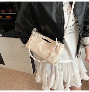 Detail of a creamy white glossy drawstring handbag with decorative knotted shoulder strap