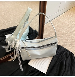 Close-up of light blue denim baguette bag featuring double zippers and a white lace bow