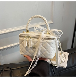 Detail of white quilted box bag featuring a woven handle and lace bow decorative element