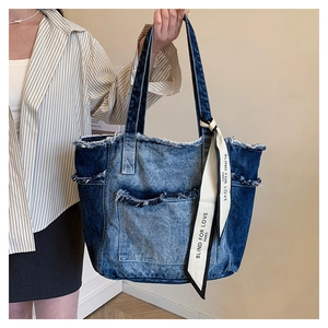 Détail d'un cabas en denim délavé color-block avec bords effilochés et ruban décoratif