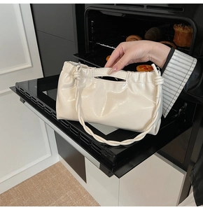 Detailed view of cream-colored pleated PU tote bag with knotted handle in a creative setting