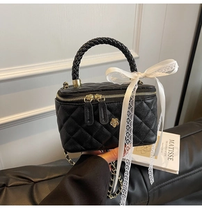 Detail of black quilted box bag with woven handle and gold flower zipper pulls