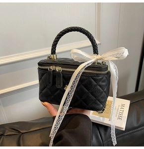 Detail of black quilted leather box bag featuring a woven handle and white lace bow