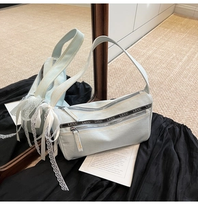 Macro shot of light blue denim baguette bag with lace bow and dual zipper details