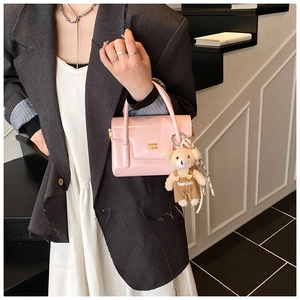 Detail of pink glossy handbag with a cute brown bear pendant in a modern setting