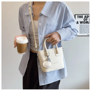 Detail einer beigen Bucket Bag aus Leder mit Herzanhänger und verstellbarem Schultergurt