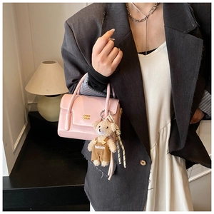 Detailed shot of pink glossy handbag featuring a golden logo and cute plush bear charm