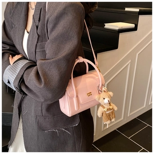 Detail of glossy pink mini handbag with golden logo and cute bear charm in natural light