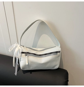 Detail of light blue denim baguette bag with silver zippers and a white lace bow charm