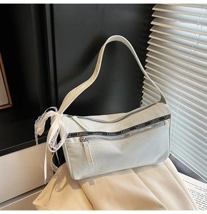 Detail of light blue denim baguette bag featuring double zippers and black branded ribbon