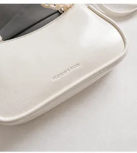 Close-up of cream white shoulder bag with pebbled leather texture and embossed logo