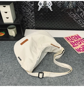 Close-up of a white nylon crescent crossbody bag with brown leather tag on felt surface
