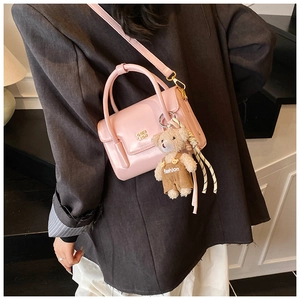 Detail of pink crossbody bag with gold hardware and a cute plush bear charm on the side