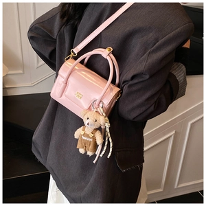 Detail of pink glossy patent leather handbag with cute teddy bear charm on cross-body strap