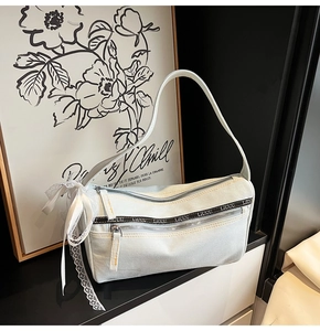Detail of light blue denim baguette bag with lace bow and metal zipper textures
