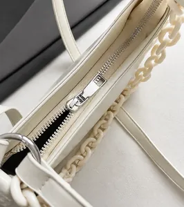 Detail of silver smooth metal zipper and resin chain on a cream crossbody bag