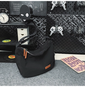 Detail of black nylon crescent bag with brown leather logo patch and wide strap