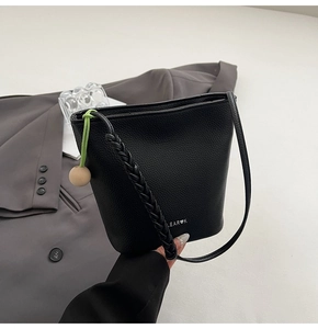 Detail of black litchi grain leather bucket bag with woven strap and wood bead charm